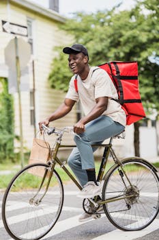 A courier smiles while delivering packages on a bicycle in an urban setting.