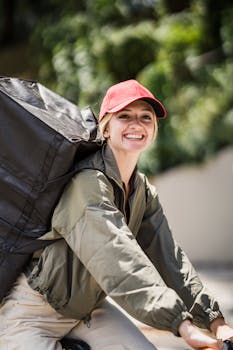 Smiling female courier riding a bike outdoors, carrying a large delivery backpack.