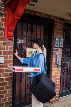 Young woman delivering pizza to a residential door, holding bags and boxes.