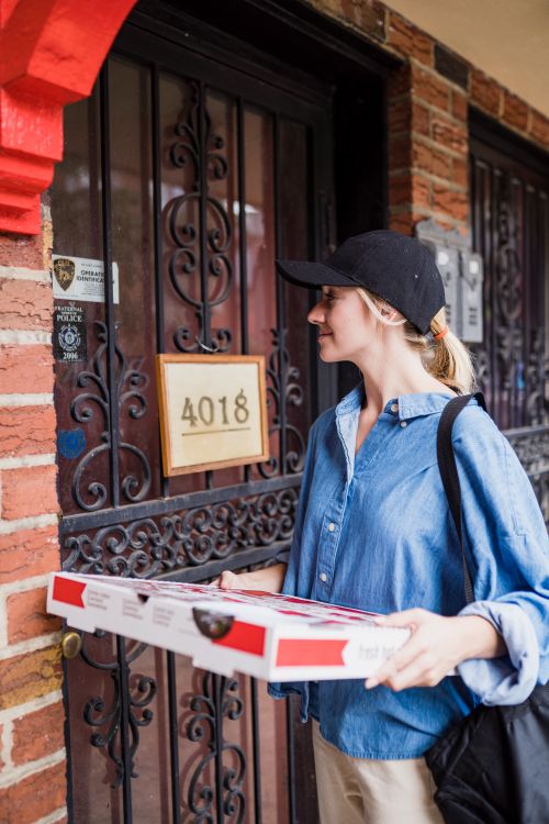 Free A delivery woman in casual attire delivers pizza to a house with ornate door. Stock Photo