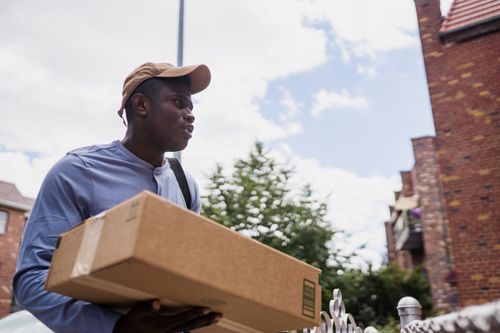 Free A man carrying a cardboard box outdoors in a residential area. Stock Photo