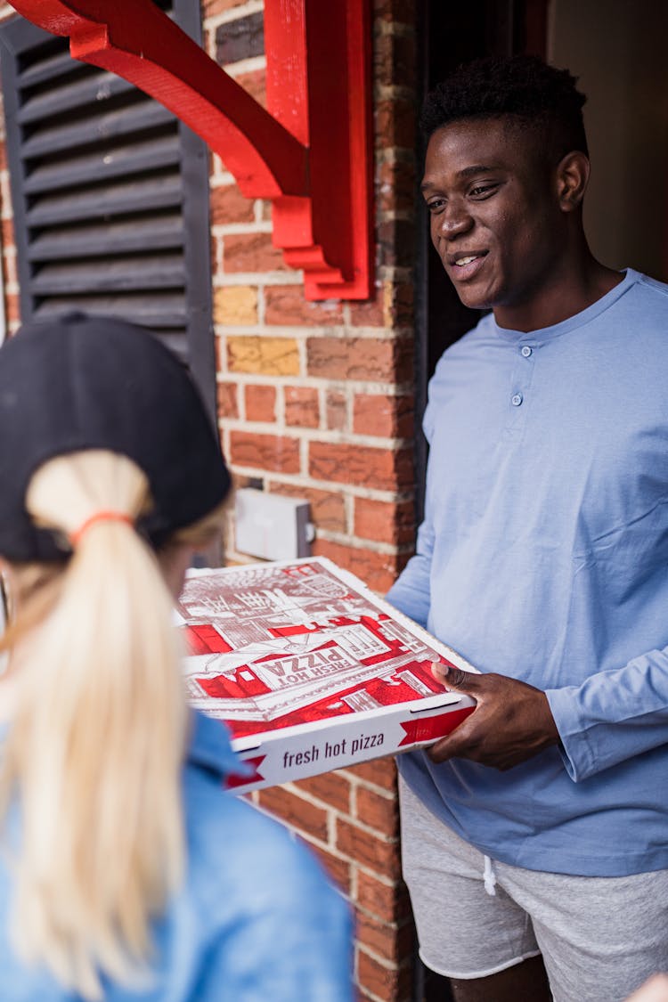 Man Holding Pizza And Talking To Woman In Doorway