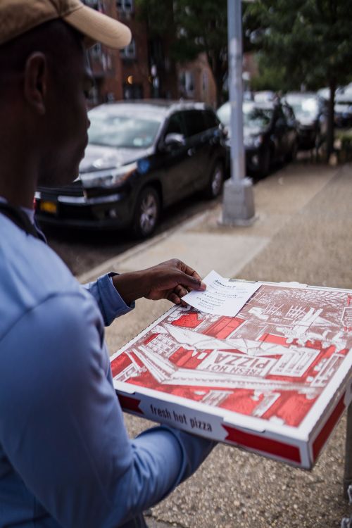 Free A delivery person carrying pizza boxes on a city street, demonstrating urban food delivery. Stock Photo