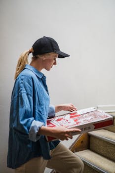 Young woman in casual attire carrying pizza boxes up a staircase indoors.