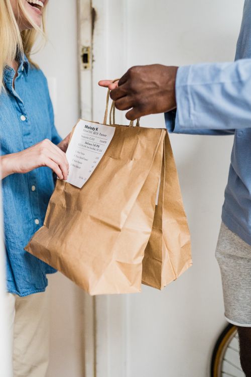 Free A smiling woman receiving a brown paper bag delivery from a man in a light indoor setting. Stock Photo