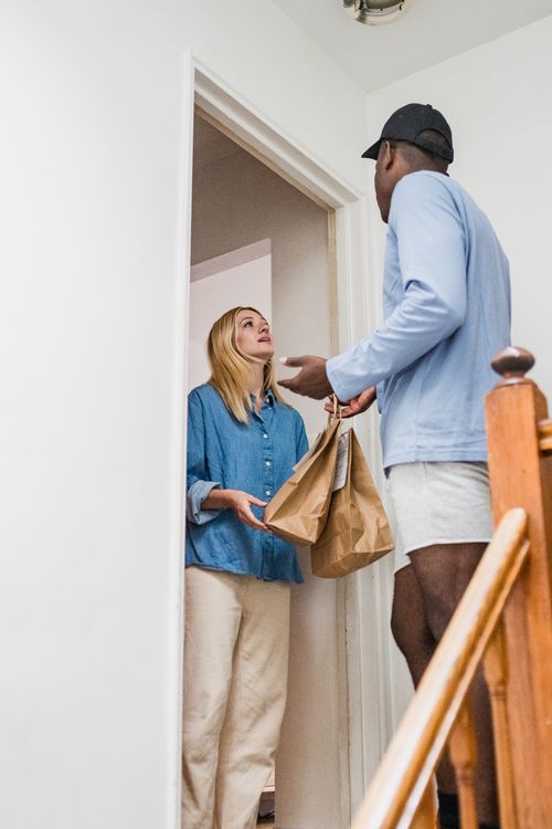 Free Two adults exchanging a package in a home's hallway, showcasing delivery service. Stock Photo