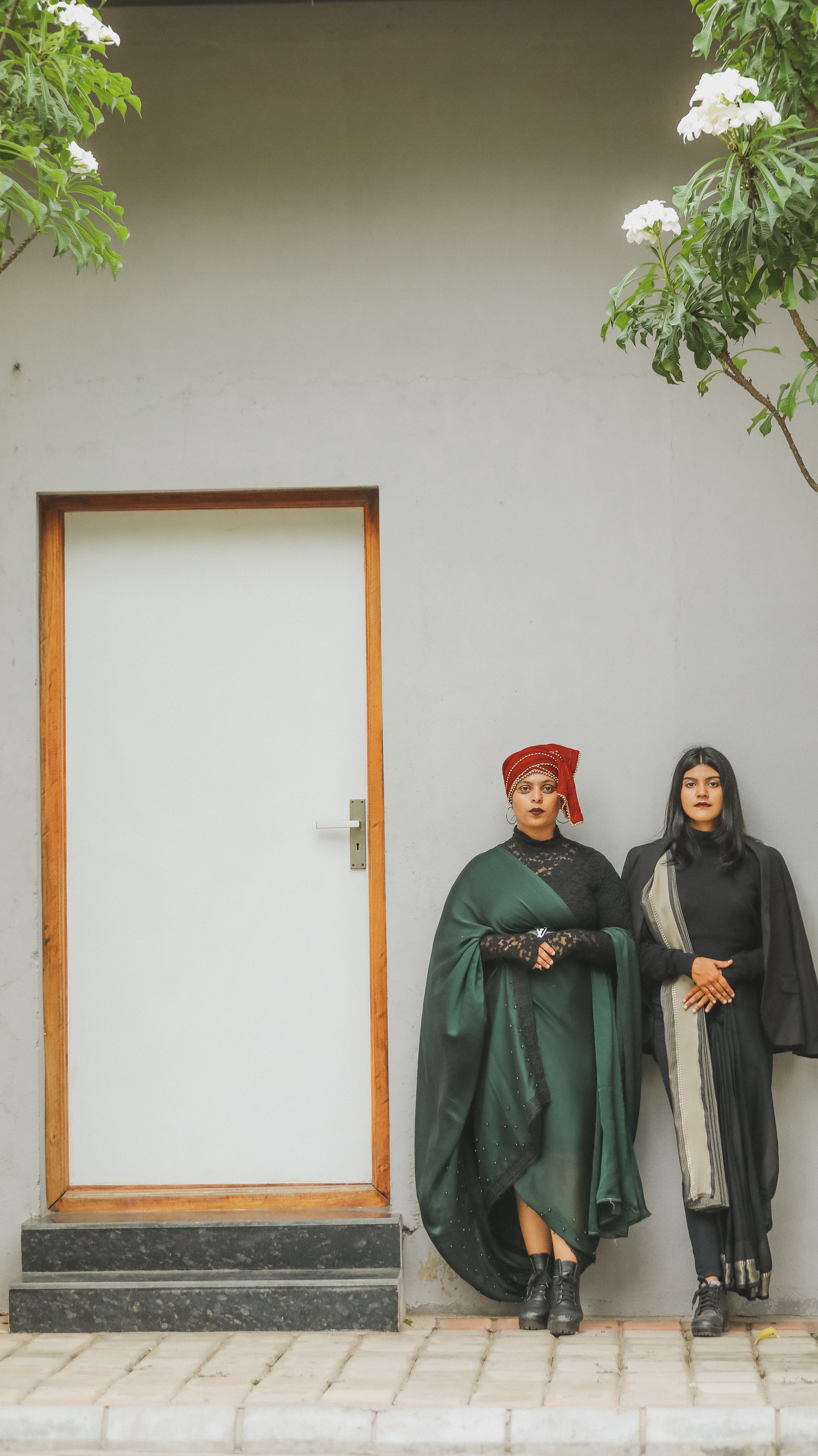 Two women in cultural outfits stand confidently by a door, embodying elegance.