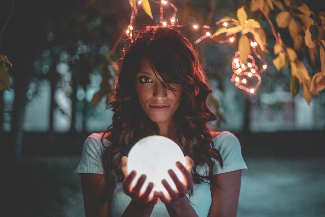 Woman Holding Lighted Glass Ball Under String Lights