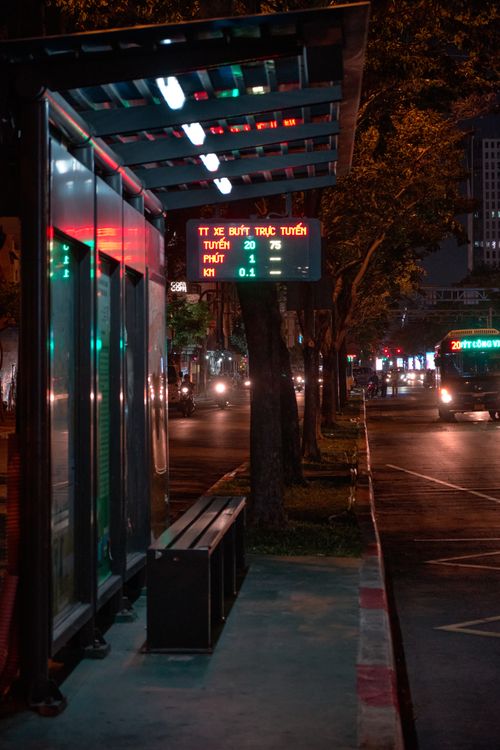 Free An illuminated bus stop at night with streetlights and cityscape in the background. Stock Photo