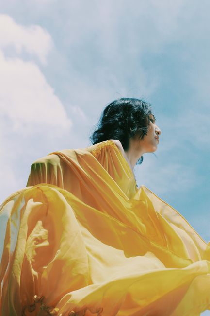 A woman in a yellow dress gazes into a sunny blue sky, capturing elegance and freedom.