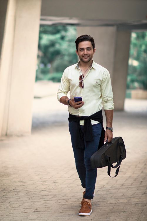 Free Young man smiling while walking with a smartphone and violin case in Tehran. Stock Photo