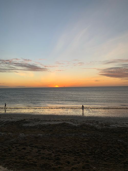 Free A tranquil beach scene at sunset with silhouetted figures walking along the shoreline. Stock Photo