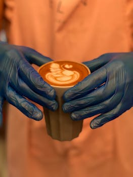 Barista in gloves holding a latte with beautiful latte art in a warm indoor setting.