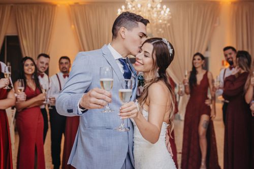 Free Newlywed couple enjoying a romantic kiss and champagne toast at their wedding celebration, surrounded by guests. Stock Photo