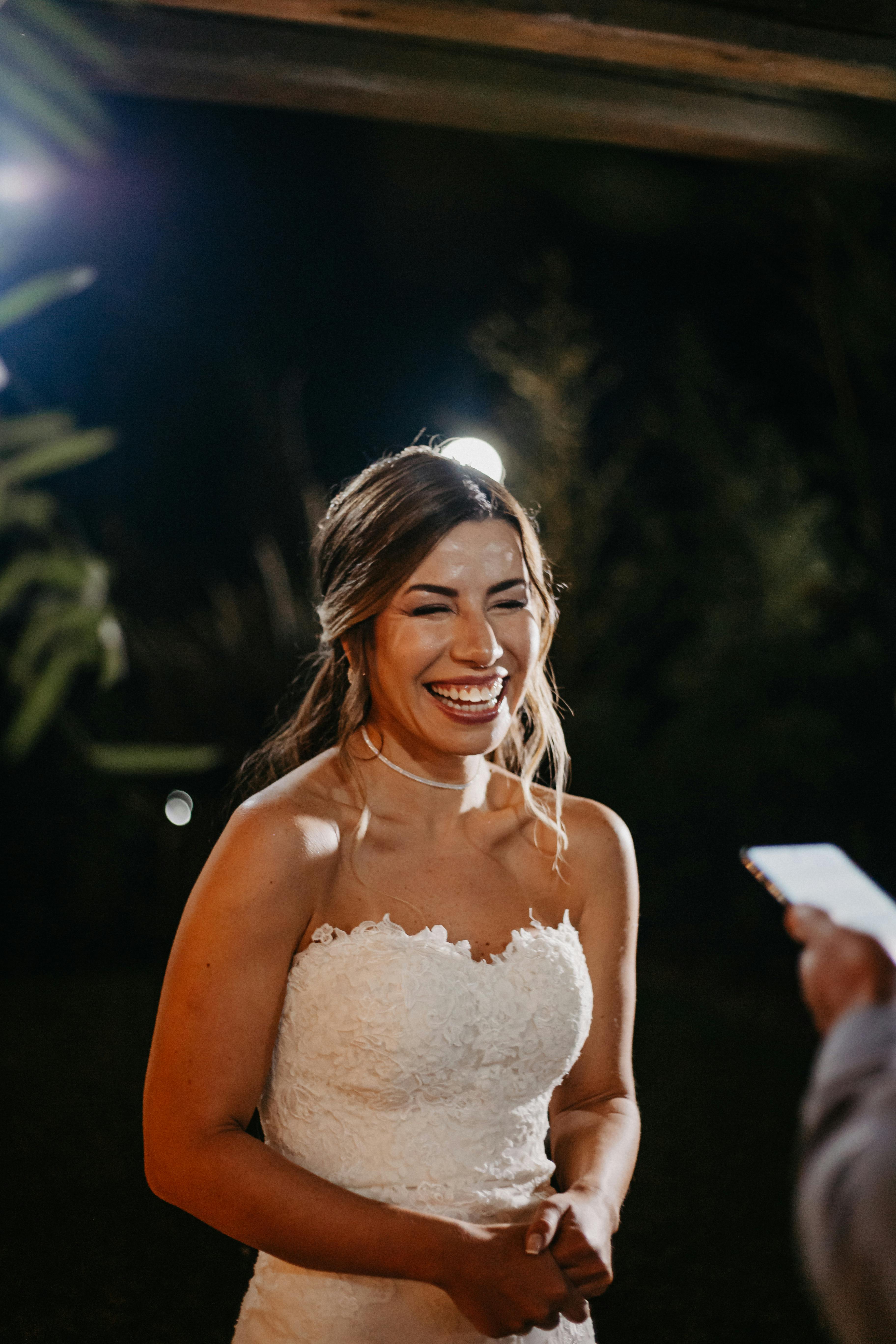 Joyful bride smiling in an elegant lace wedding dress during a night wedding ceremony.