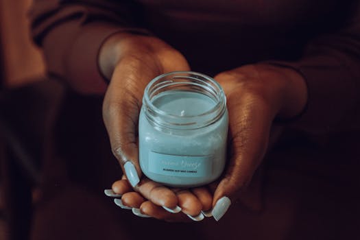 A close-up shot of hands holding a blue scented soy candle in Kampala, Uganda.