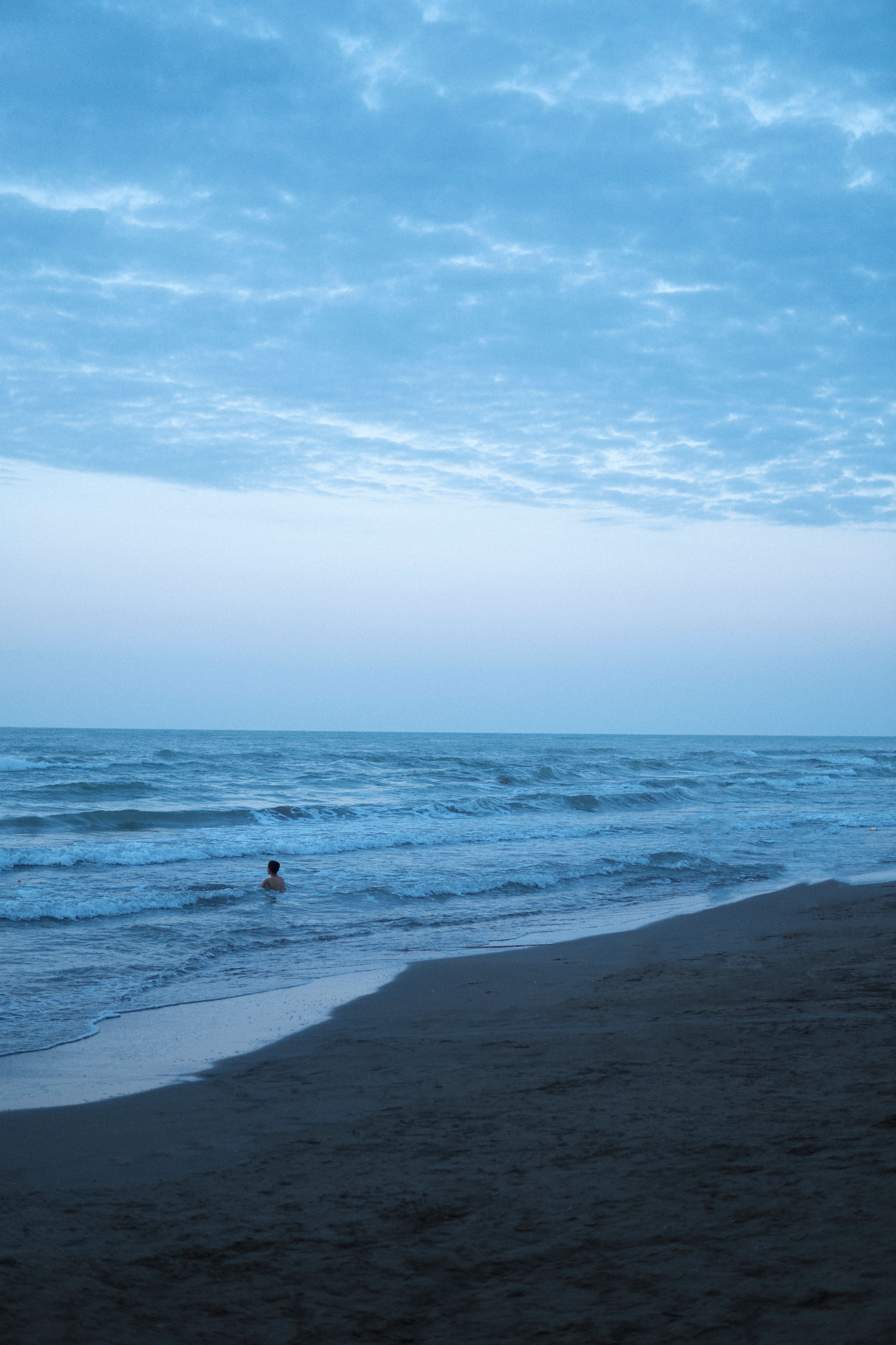 A lone swimmer enjoys the calm waves of the Caspian Sea under a cloudy sky in Mazandaran, Iran.