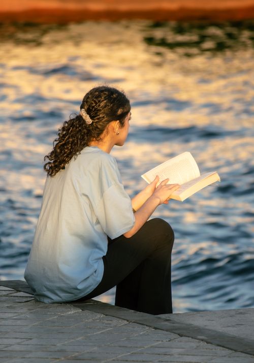 Free A woman with curly hair sits by the Bosphorus, Istanbul, enjoying a book at sunset. Stock Photo