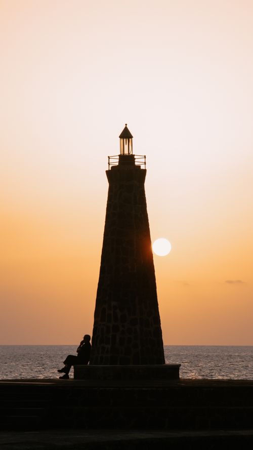 Free Silhouette of a lighthouse and person against a sunset in Bajamar, Spain, with the sun setting over the sea. Stock Photo