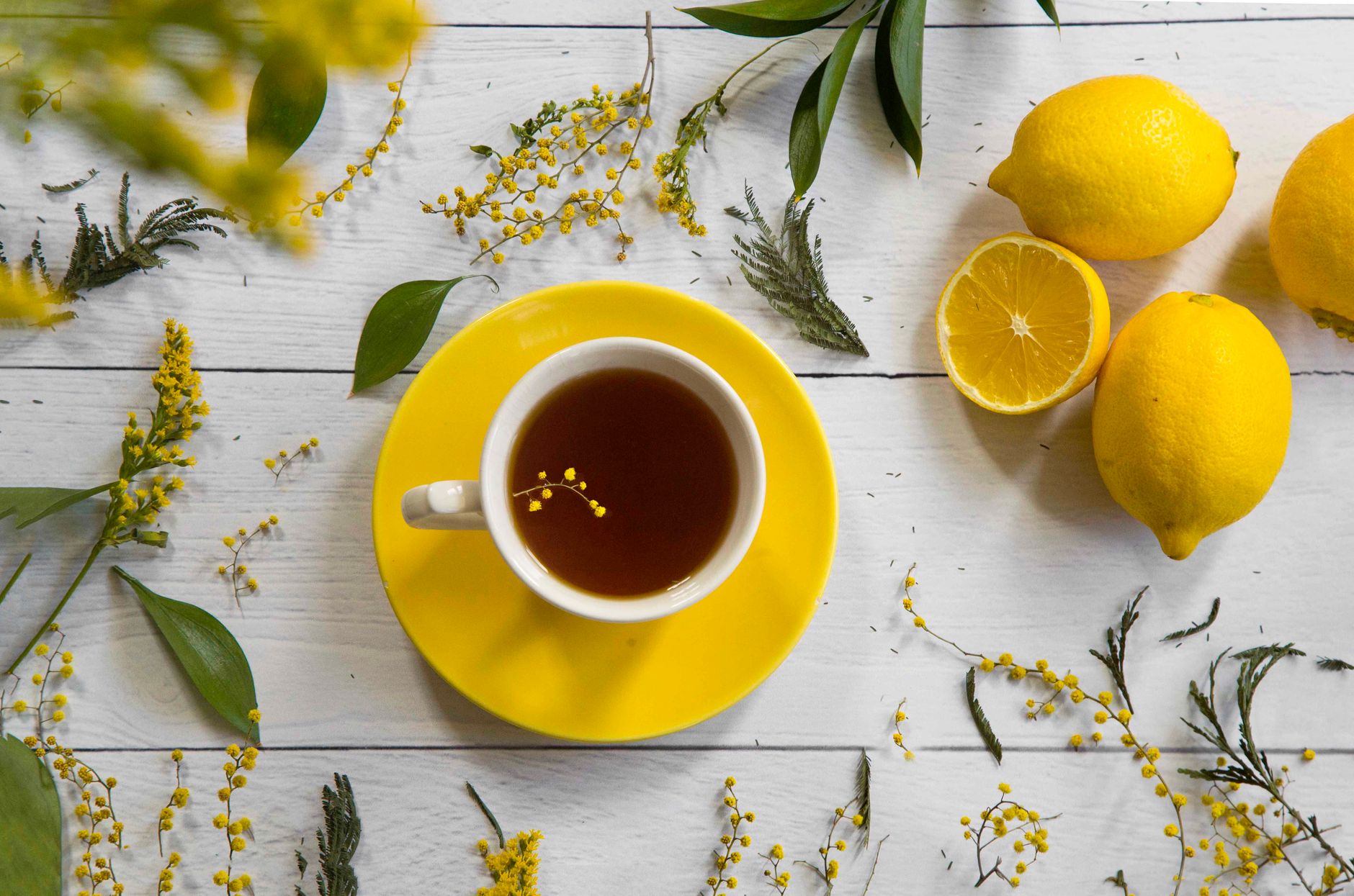 A vibrant flat lay of lemon tea with yellow flowers and citrus fruits on white.