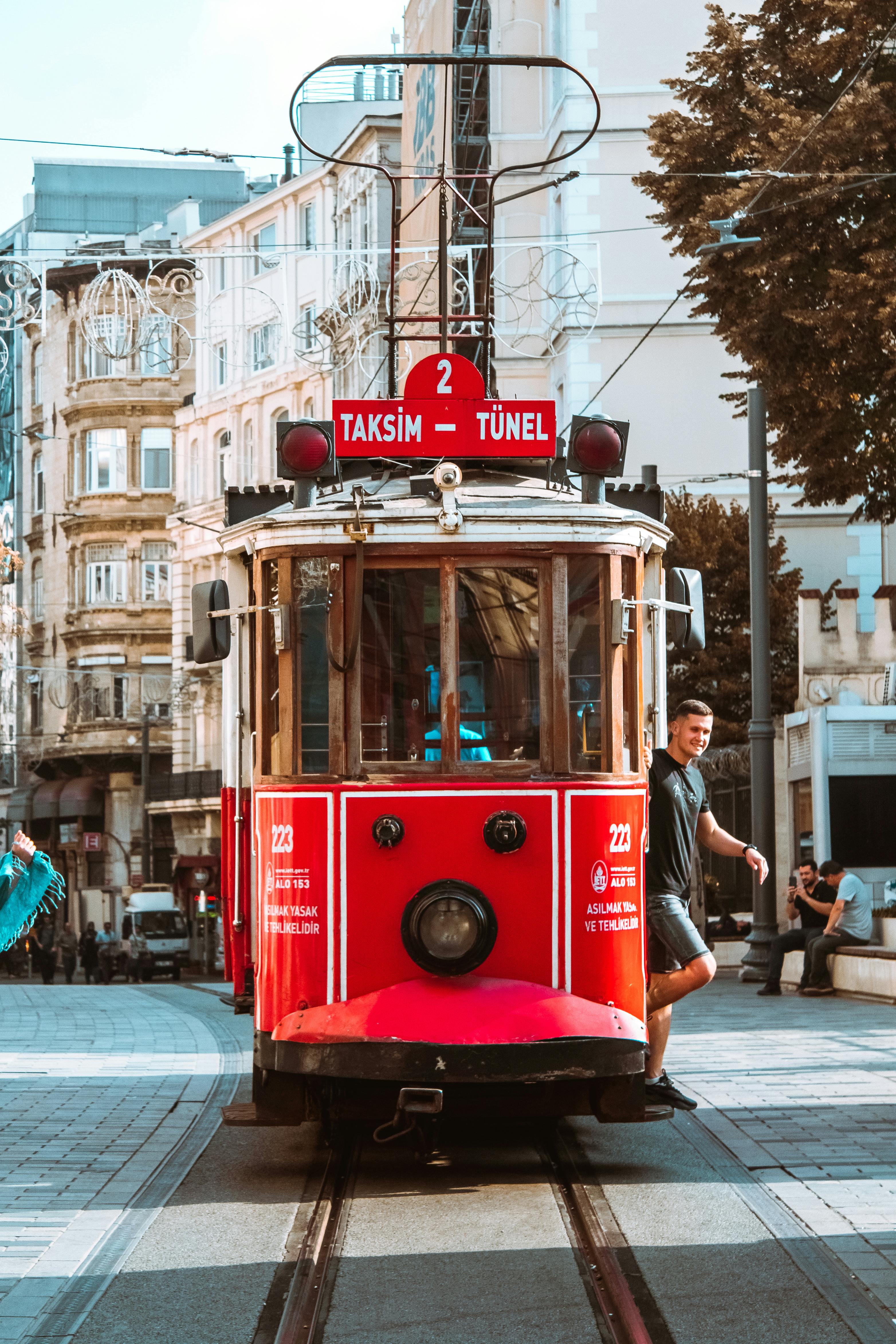 Vintage red tram in Istanbul's Taksim Square on a sunny day, highlighting urban transport charm.