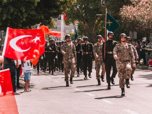 Free Soldiers marching in a Turkish military parade, waving national flags in a tree-lined urban setting. Stock Photo