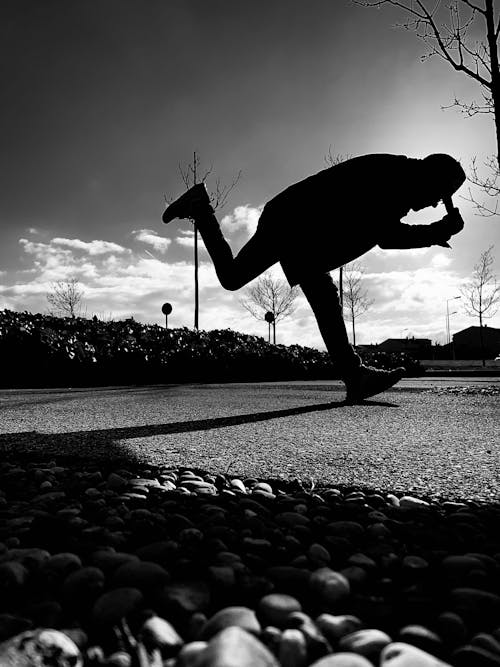 Grayscale Photo of a Person Standing on Concrete Road