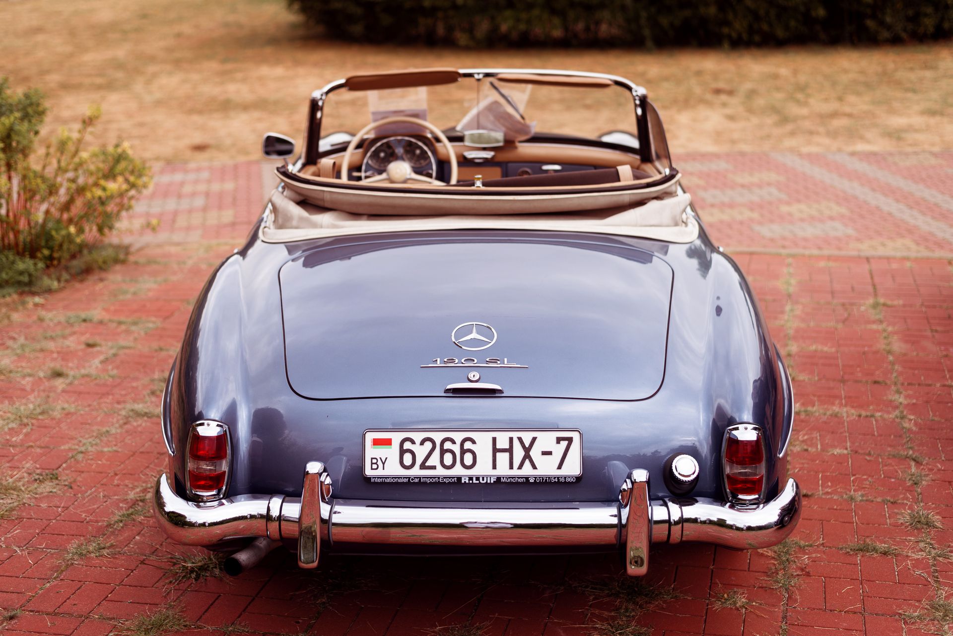 Rear view of a classic Mercedes Benz 190 SL parked on a brick driveway.