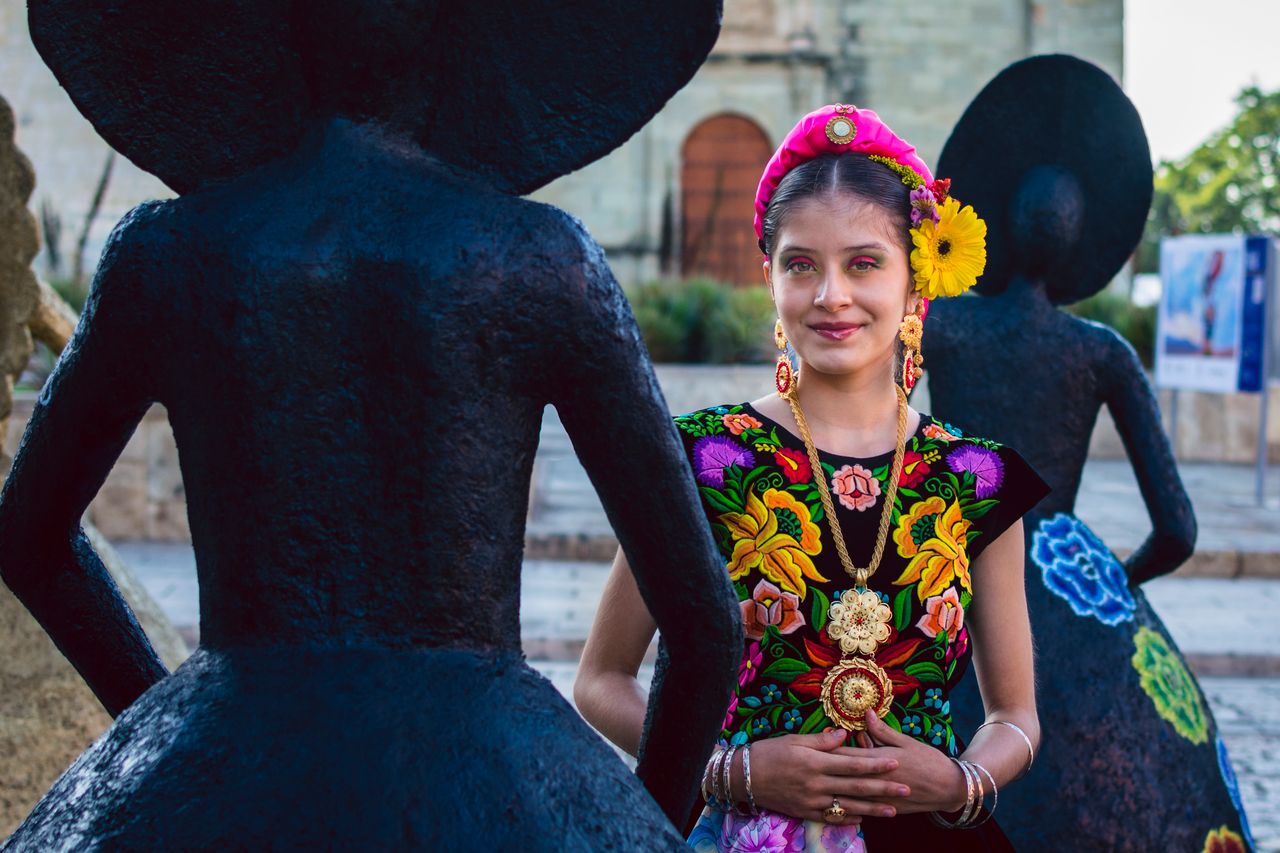 smiling woman in traditional zapotec attire surrounded by black statue