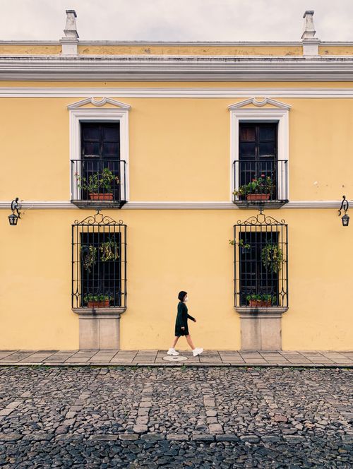 Free Woman walking by a yellow colonial building on a cobblestone street in Antigua Guatemala. Stock Photo