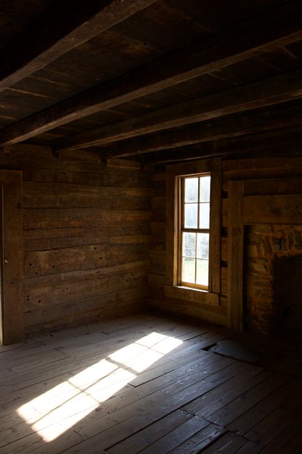 Empty wooden cabin interior with sunlight streaming through window, highlighting rustic charm.