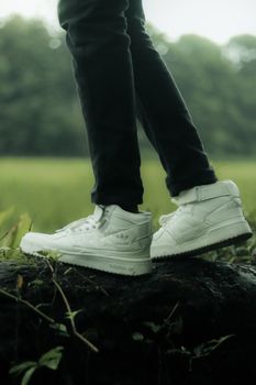 Stylish white sneakers on a rock in nature, highlighting fashion and outdoor lifestyle.