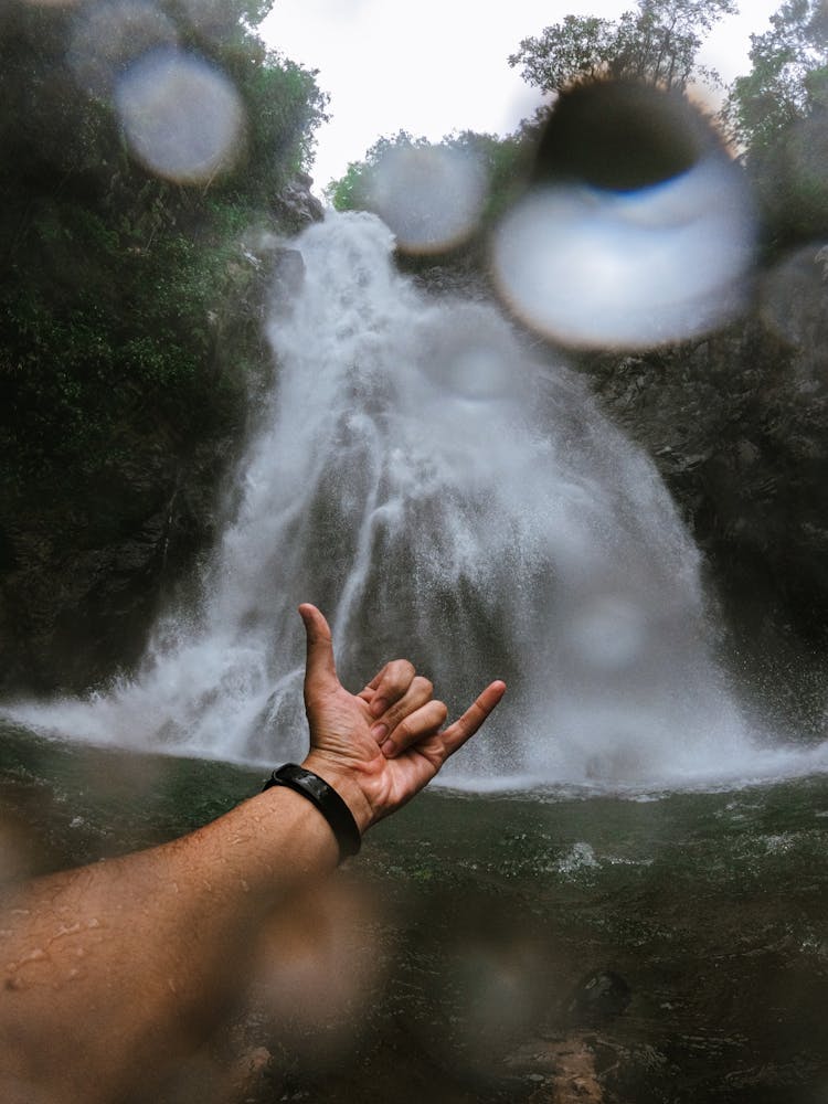 Hand Gesture Of Devil Horns With Waterfall In Background