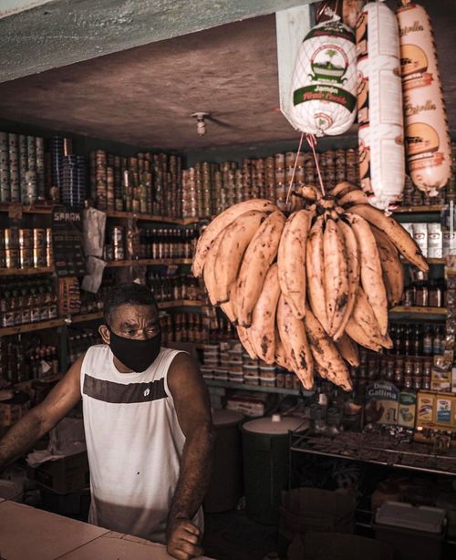 Free Man wearing mask in a Santo Domingo local store surrounded by merchandise and hanging produce. Stock Photo