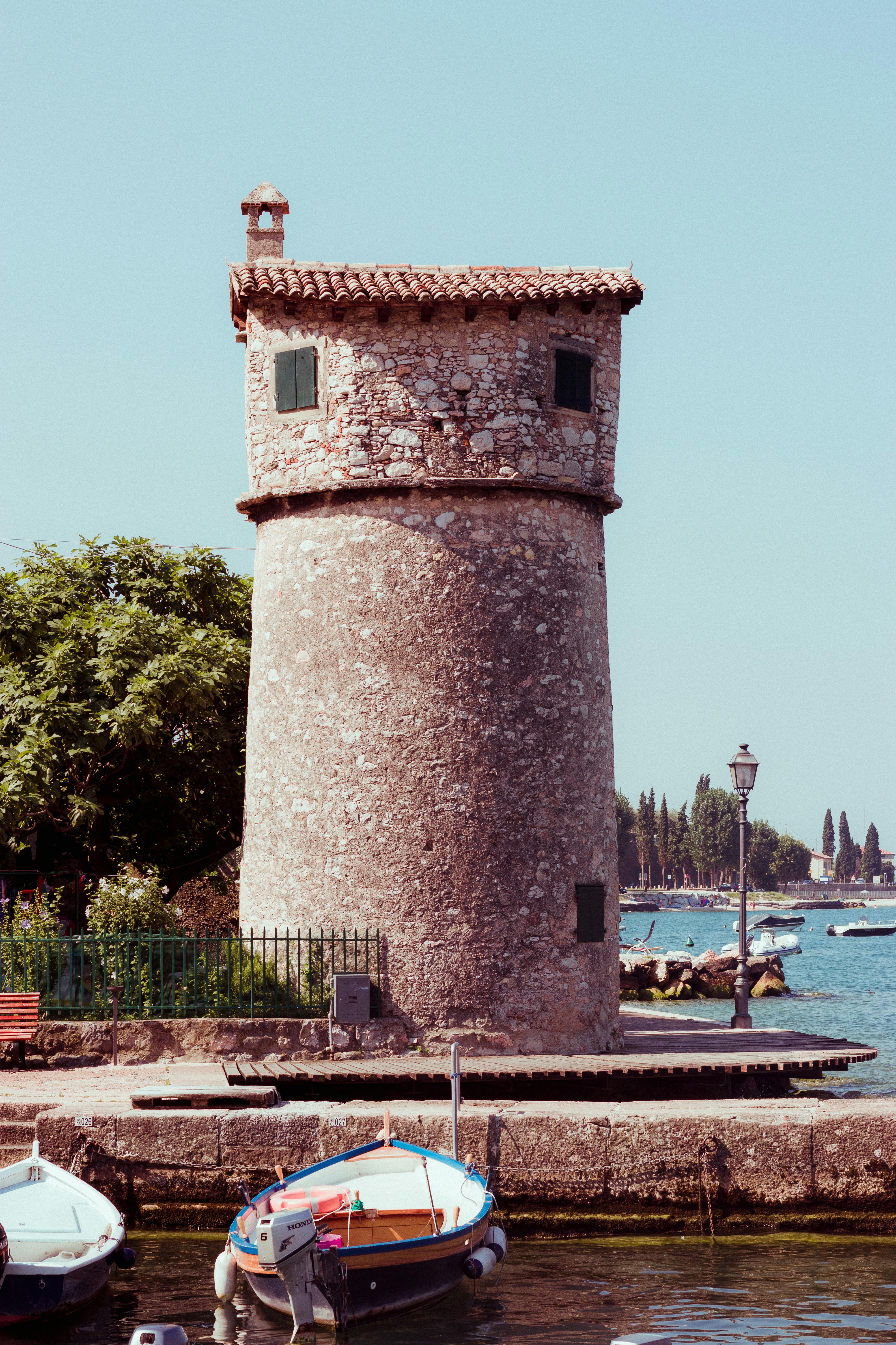 意大利加尔达湖畔马尔西的迷人石塔，风景优美的海滨景观中点缀着船只与树木