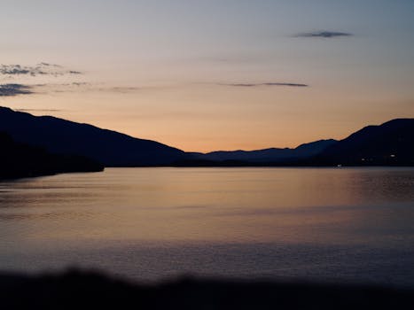 A tranquil lake view at twilight with silhouetted mountains in the background.