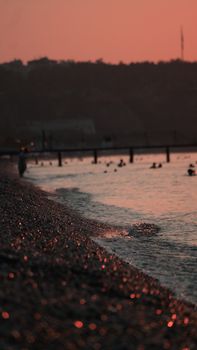 A tranquil beach scene with pebbles and people enjoying the water at sunset.