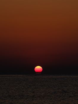 Stunning view of a red sun setting over dark ocean waters, creating a dramatic and tranquil scene.