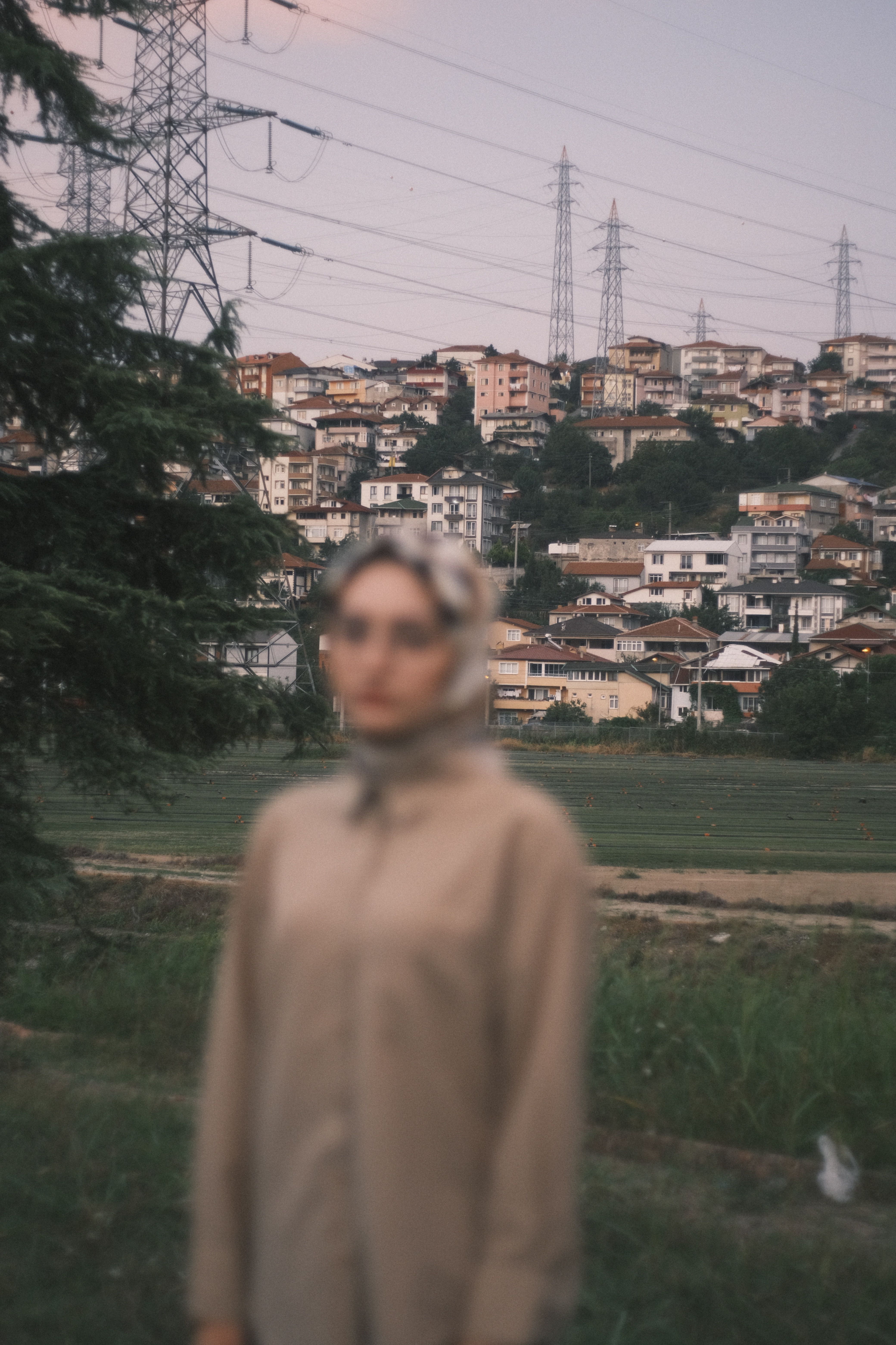 An artistic photo featuring a blurred woman in front of a hillside cityscape with power lines at dusk.