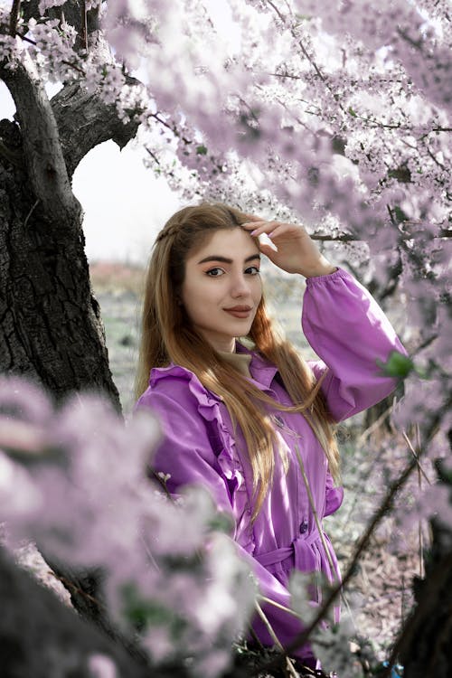 Woman in Purple Long Sleeve Shirt Standing Beside a Flowering Tree