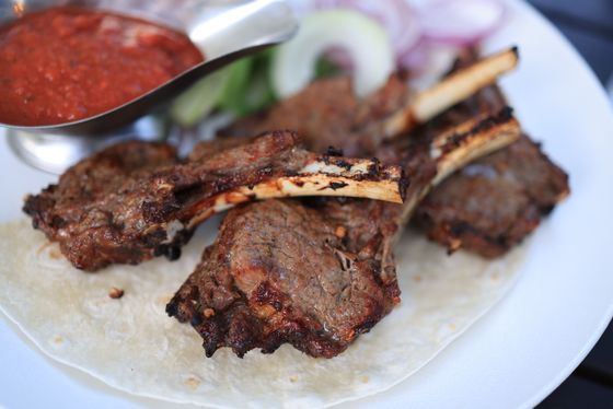 Charred bone-in lamb chops on thin flatbread with red pepper sauce, cucumber and onion slices
