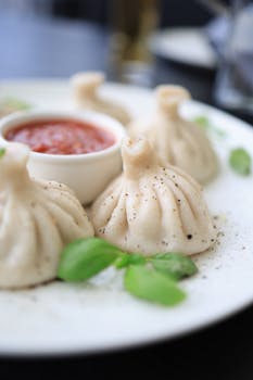 Close-up of khinkali dumplings with a side of spicy tomato sauce on a plate.