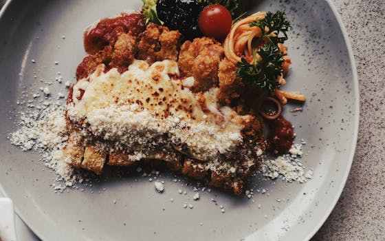 Crispy chicken parmigiana topped with cheese and tomato, served with spaghetti on a plate.
