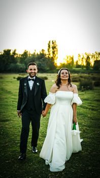 Charming couple smiles in outdoor wedding setting, holding hands under sunset light.