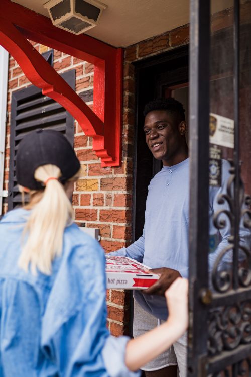 Free Man receiving a pizza delivery at a brick house entrance. Stock Photo