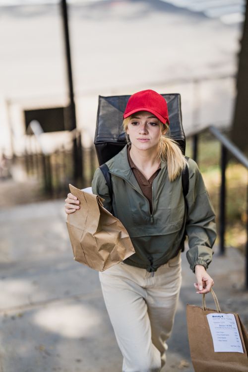 Free A woman in casual attire delivering food outdoors, holding paper bags. Stock Photo