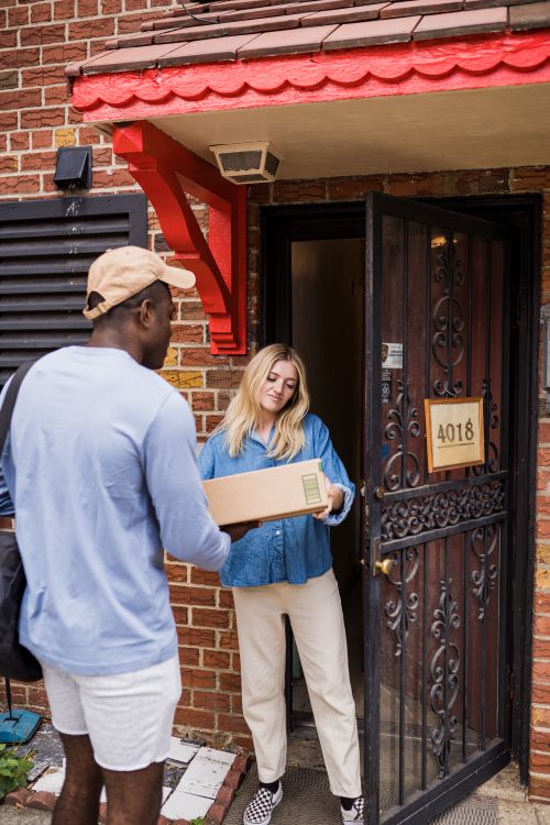 Free Man delivering parcel to woman at home entrance, showcasing modern courier service. Stock Photo