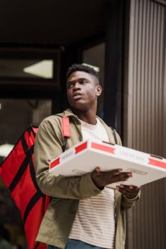 A delivery person holds pizza boxes outdoors with a red backpack, ready for delivery.