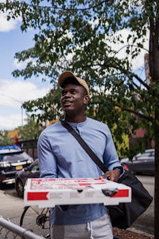 Portrait of deliveryman with pizza box walking on a city street, capturing the urban lifestyle.
