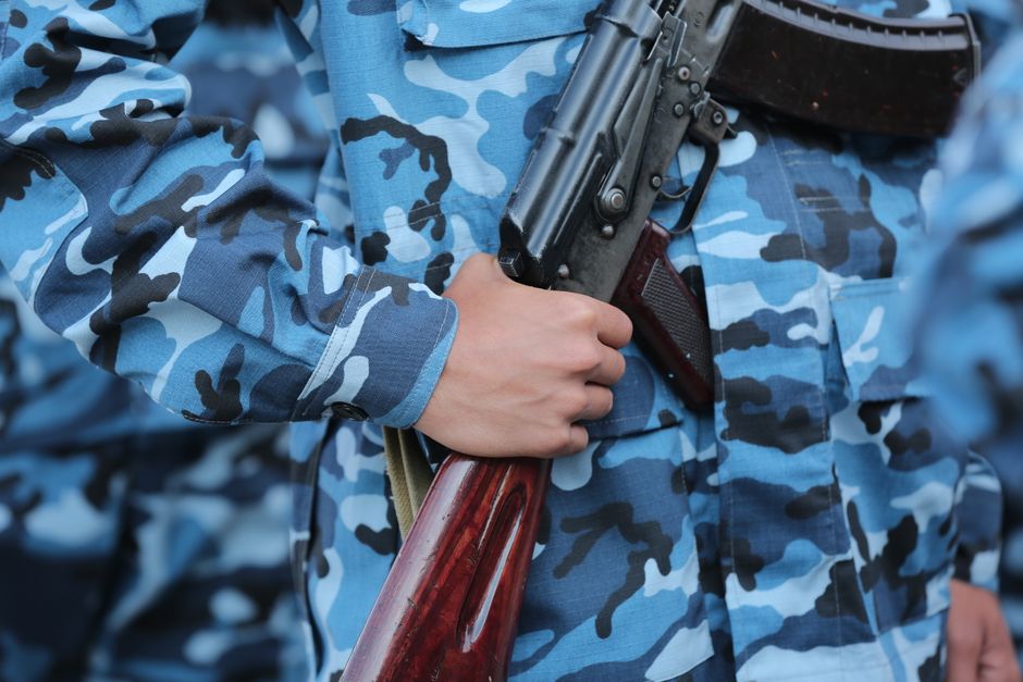 Close-up of hand holding a rifle in blue camouflage uniform, outdoors.